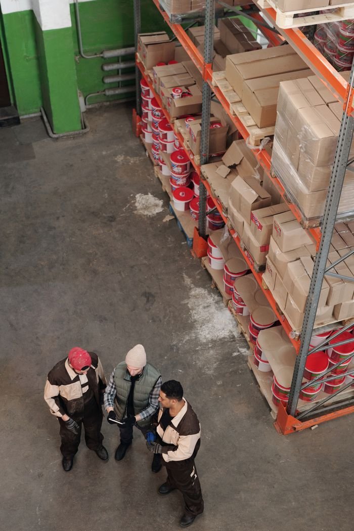 Facture électronique Peppol : ce que les restaurants, snacks et épiceries doivent savoir Group of warehouse workers discussing logistics and inventory in a large storage area with shelves and packages.